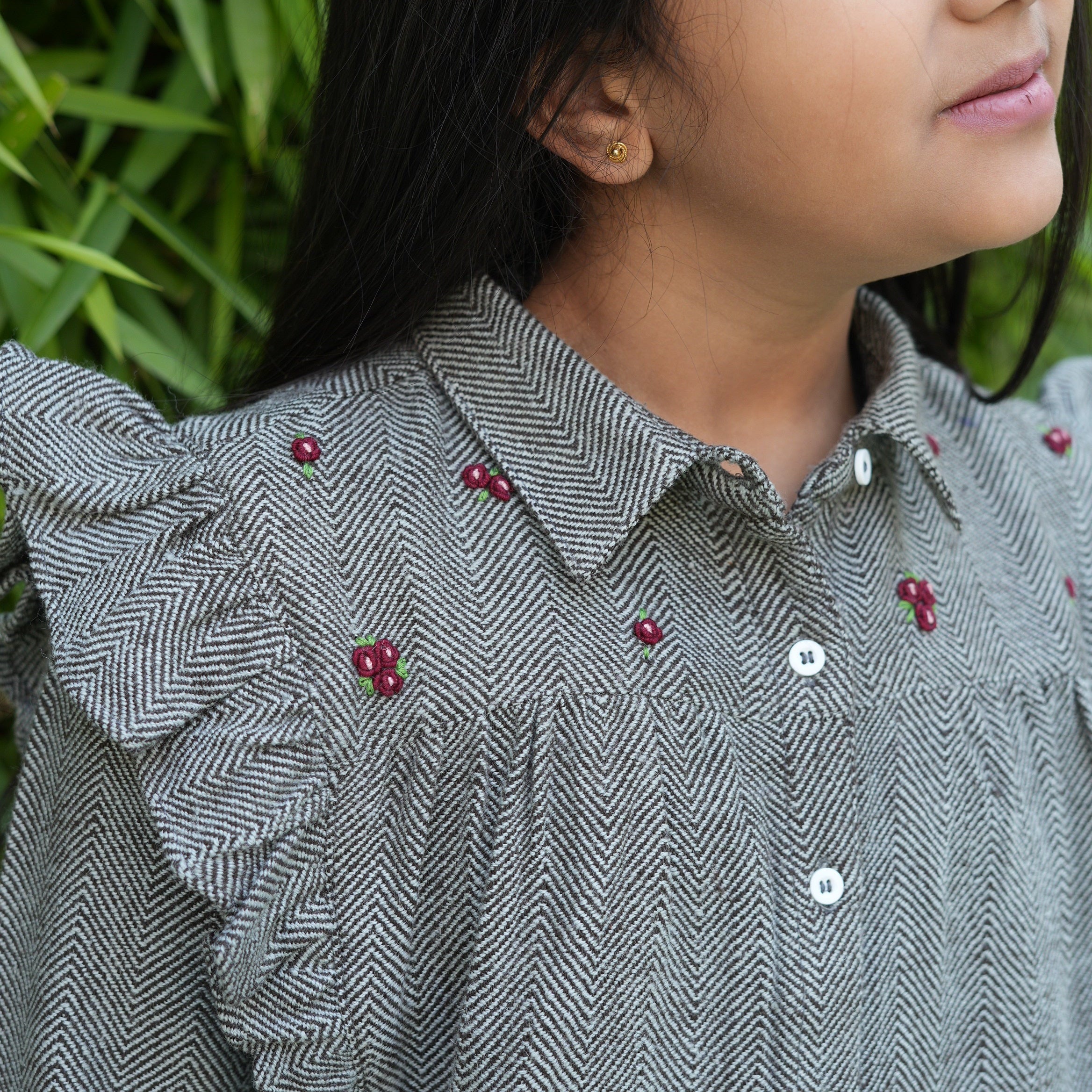Young girl wearing a grey button-down ruffle shirt from The Little Trunk.
